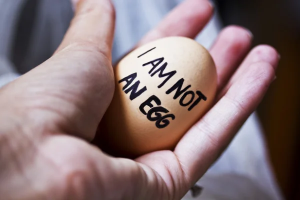 An egg in the palm of a man. On the egg is written 'I am not an egg'.