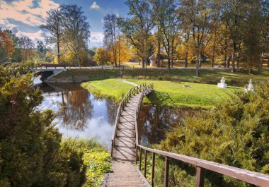 Nehir, göl veya göl üzerinde ahşap köprüsü olan sonbahar renkli bir park.
