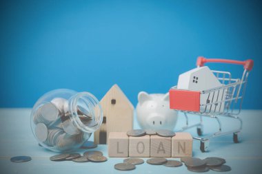 Mini bir ahşap ev modeli alışveriş arabasında ve mavi bir masanın üzerindeki tahta bloklarda yazılı kredisi var. Gayrimenkul ticareti fikirleri, gelecek için tasarruf, bankacılık, finans ve muhasebe.