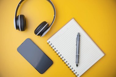 Teknoloji, rahatlamak için multimedya müzik. Üst manzara, düz yatış. Siyah beyaz bir kulaklık üzerinde akıllı telefon olan bir defter ve kopya alanı olan sarı bir arka plan..