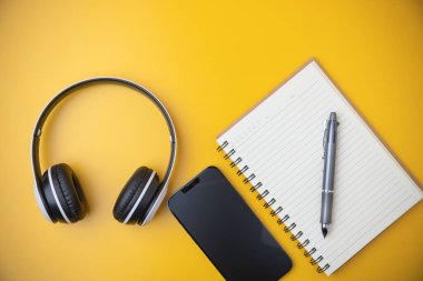 Teknoloji, rahatlamak için multimedya müzik. Üst manzara, düz yatış. Siyah beyaz bir kulaklık üzerinde akıllı telefon olan bir defter ve kopya alanı olan sarı bir arka plan..
