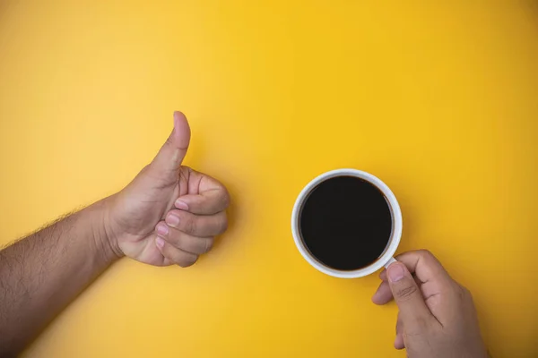Morning drinks coffee. top view espresso coffee break. Hand of a man holding a white cup with hot black coffee on yellow background with copy space.