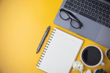 İş, teknoloji, eğitim ve öğrenme konsepti. Ofis çalışma alanı sarı masa masasında laptoplu, kahveli, kalemli, defterli, bitkili alanı kopyala. sarı arka planda düz döşeme ekipman ofisi.