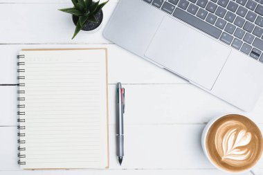 Top view with copy space, flat lay. Top view white office desk table with a blank notebook, a pen, a laptop, and a cup of coffee on old white wooden background. Business office, technology concept.