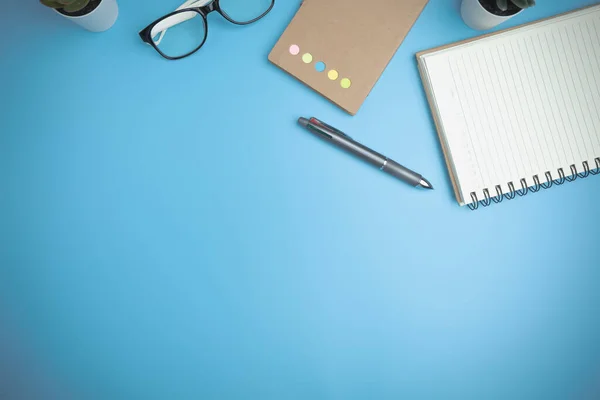 The blue office desk with a notebook, a pen, glasses, and a mini tree. Office table desk of the business flat lay, background. Top view workspace of table office with copy space. Business concept.