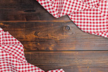 Checkered red and white tablecloth on an old wooden brown background with copy space. Flat lay, top view. Background of menu for the restaurant, copy space. Fabric red and white cover on the table.