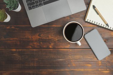 Top view desk of work office with laptop, smartphones, a pen, green leaf, and coffee of cup on old wooden background with copy space. Flat lay, top view. Old wood office table. 