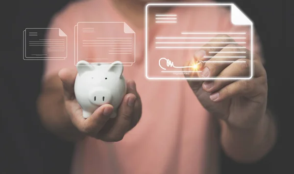 A man using a pen signs in virtual electronic documents with a white piggy bank on hand. Security cyber and paperless technology concepts.