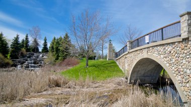 İlkbaharda şelale geçmişi olan bir parktaki nehir üzerinde köprü.