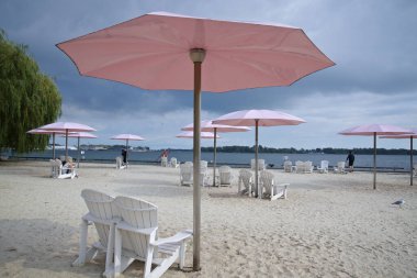 Toronto, Ontario / Kanada - 12 Eylül 2022: Pembe plaj şemsiyeleri ve güneşli göl kıyısındaki Adirondack sandalyeleri