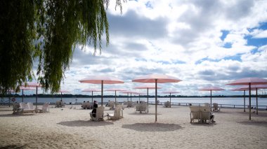 Pembe şemsiyeli ve Muskoka sandalyeli bir sahil parkı. 