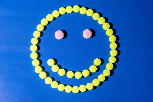 Смайлі з жовтих таблеток на синьому фоні — стокове фото