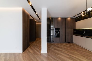 Stüdyo mutfağının içinde aydınlık duvarlar ve koyu renkli mobilyalar var.