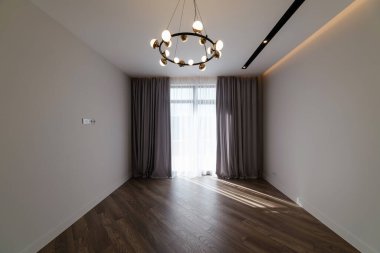 Evin içinde büyük bir penceresi, avizesi ve zemini olan beyaz bir oda.