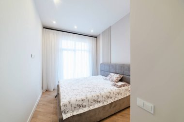 Karanlık zeminli büyük yataklı ve pencereli bir oda.