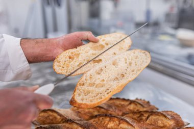 Bir adam büyük bir bıçakla kesiyor taze pişmiş ekmek tüketime hazır.