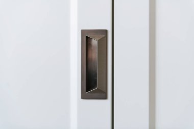 Beyaz ahşap bir dolapta metal, siyah bir kapı kolu var.