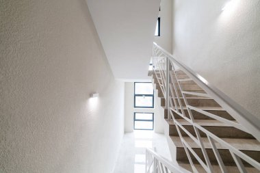 Koridorun içinde beyaz metal parmaklıklar ve merdivenler var.