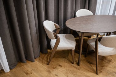 Büyük Pencere 'nin yanında perdelerle çevrili koyu renkli ahşap masa ve hafif sandalyeler.