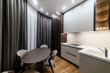 Masası ve sandalyeleri olan bir mutfak. Büyük perdeler ve pencereler