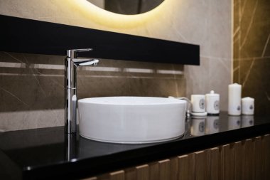 Modern banyo tasarımı beyaz lavabo metal musluğu ve arka lambası var.