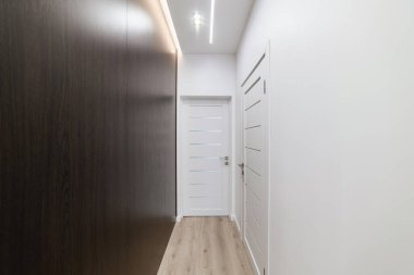 İçerisi aydınlık, karanlık duvar ve beyaz kapılarla dolu.