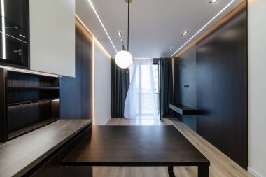 Kahverengi duvarı, siyah mobilyası ve geniş penceresi olan geniş bir mutfak stüdyosu.