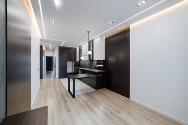 Beyaz duvarı ve koyu renkli mobilyası olan ferah bir mutfak.