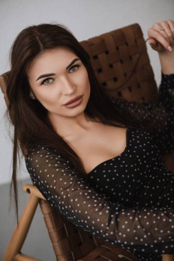 Koyu renk elbiseli esmer bir kız sandalyede oturuyor.