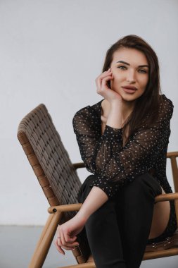 Kız kahverengi bir sandalyede oturuyor ve fotoğraf için poz veriyor.