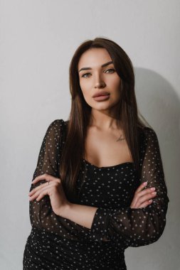 Koyu tenli, siyah elbiseli, kolları katlanmış bir kız.