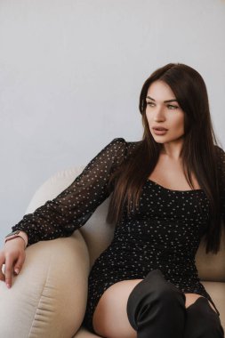 Siyah elbiseli kız beyaz sandalyede oturuyor.