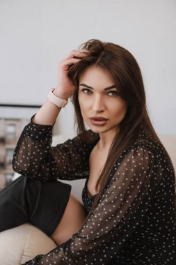 Siyah saçlı kız model elini başının yanında tutuyor.