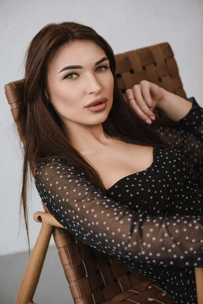 Koyu renk elbiseli esmer bir kız sandalyede oturuyor.