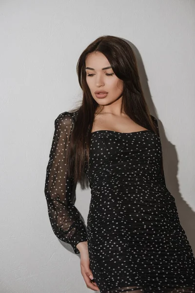 Siyah elbiseli kız beyaz arka planda poz veriyor. Aşağı bak.