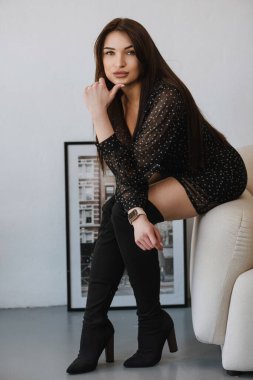 photo of a girl in dark clothes and high shoes on a white chair