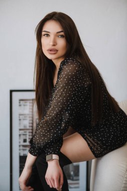 Siyah saçlı, siyah elbiseli, sandalyede oturan bir reçine kızı.