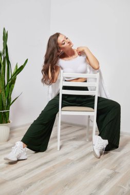 Şık kıyafetler içinde bir sandalyede oturan bir fotoğrafçıya poz veren bir model.