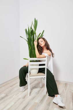 tanned girl sitting on a chair with open eyes near the plant