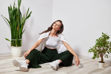 tanned girl sitting on the ground near the plant