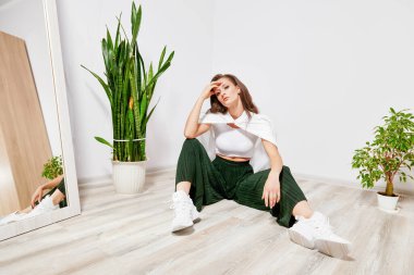 young girl in green pants and a white shirt sitting on the floor