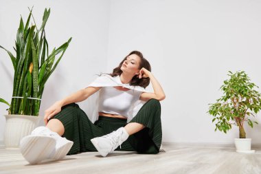 girl in stylish clothes sitting on the floor near the plant