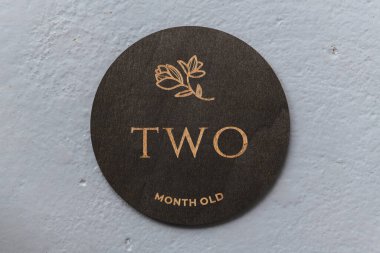 Koyu ahşap yuvarlak tahta üzerinde gri arka planda iki yazıt var.