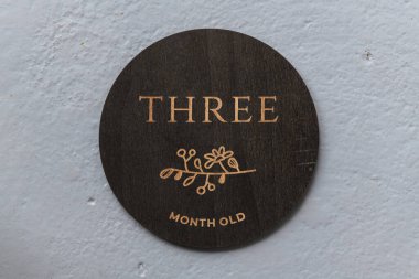 Koyu ahşap yuvarlak tahta üzerinde gri arkaplanda üç yazılar var.