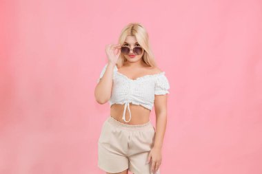 Pembe arka planda açık renk elbiseli ve gözlüklü genç bir kız.