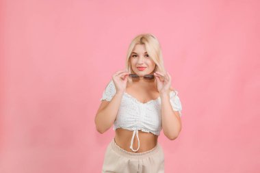 Pembe arka planda açık renk elbiseli ve gözlüklü genç bir kız.