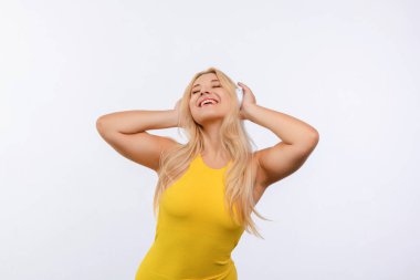 Beyaz saçlı, sarı elbiseli genç ve güzel bir kız beyaz arka planda müzik dinliyor.