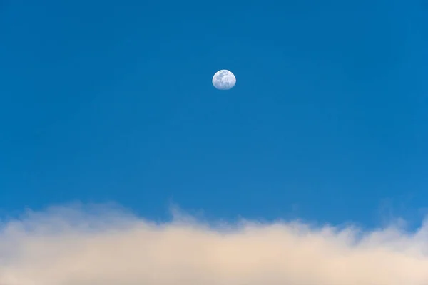 Day moon and strange clouds on the blue sky