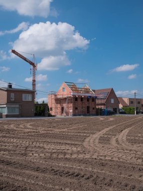 Sint Gillis Waas, Belçika, 29 Mayıs 2022, inşaat halindeki bir ev, etrafında iskele, beyaz bulutlu mavi gökyüzü ve ön planda yeni sürülmüş bir tarla.