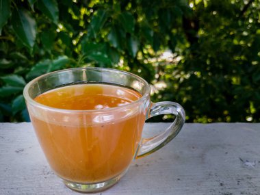 Arka planda yeşil ağaçlar olan şeffaf bir fincanda izole edilmiş yeşil çay.